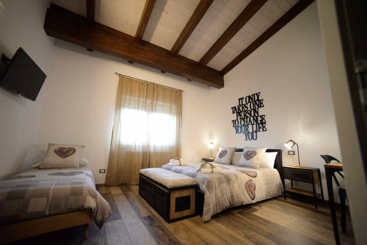 A bedroom with a large bed, a smaller bed, a nightstand, a lamp, and a wall with a motivational quote.
