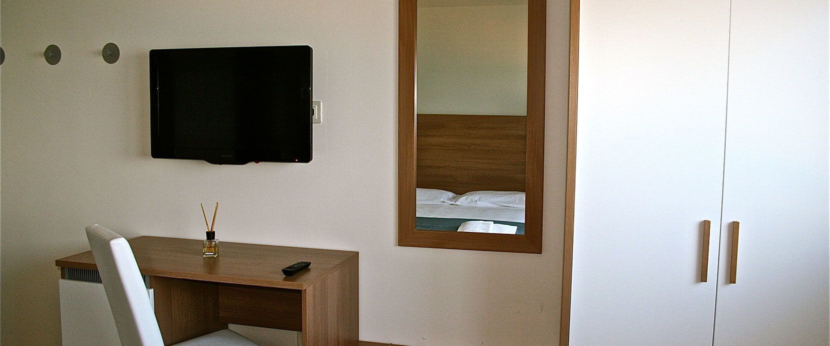 Habitación de hotel con un escritorio de madera, una silla, un televisor de pantalla plana montado en la pared, un espejo y un armario con dos puertas.