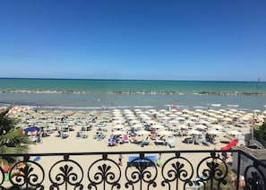 A beach with numerous sun umbrellas and lounge chairs, a rocky breakwater, and a clear blue sky. - Baia Marina Hotel (Cupra Marittima)