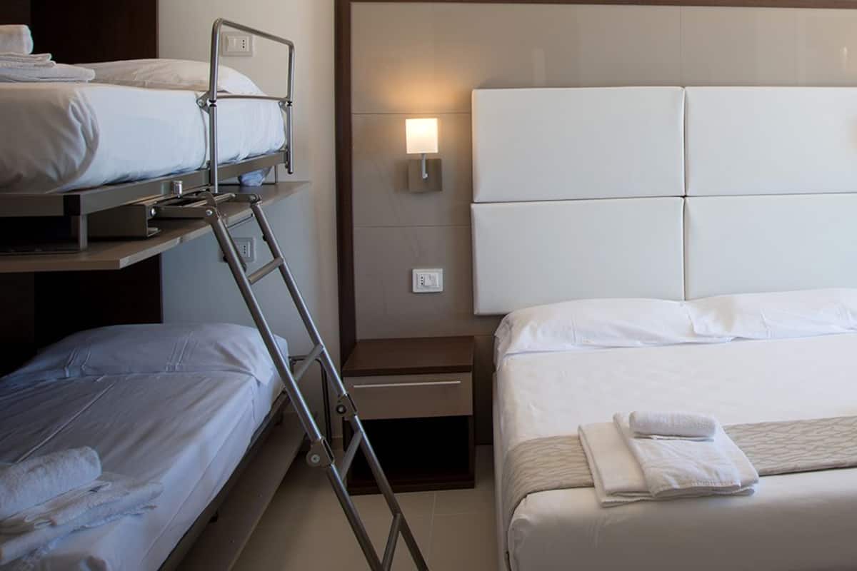 Une chambre d’hôtel avec un grand lit, un lit plus petit et un lit superposé. Il y a des tables de chevet avec des lampes et une fenêtre donnant sur un beau paysage.
