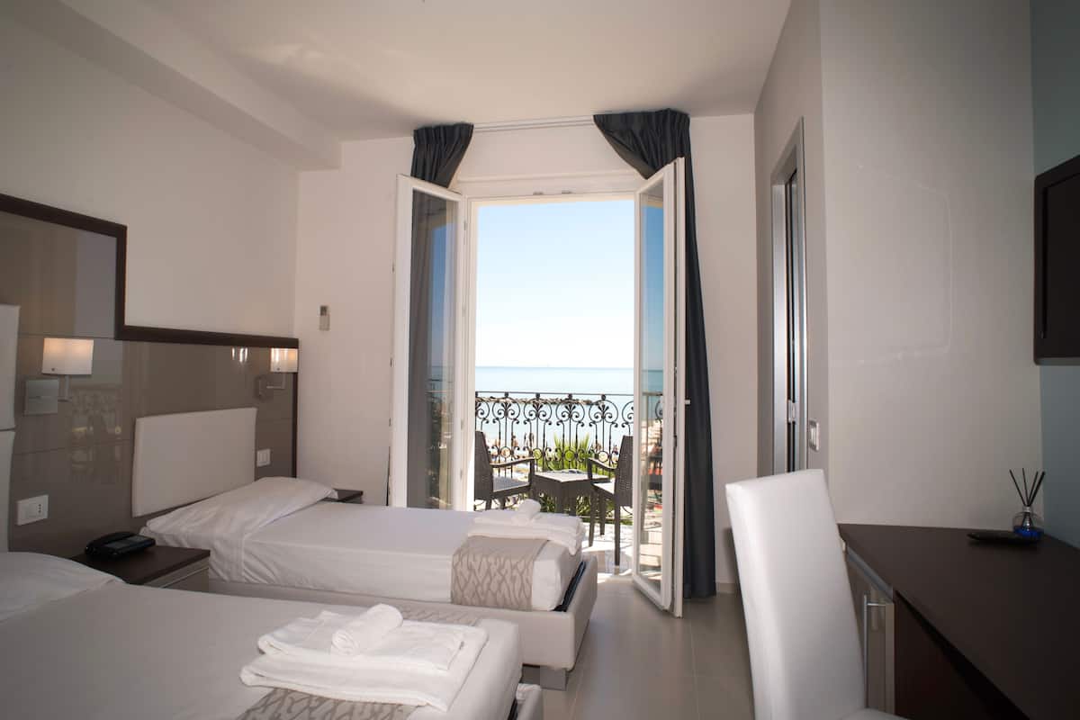 Une chambre d’hôtel avec deux lits, un bureau et un balcon donnant sur la mer.
