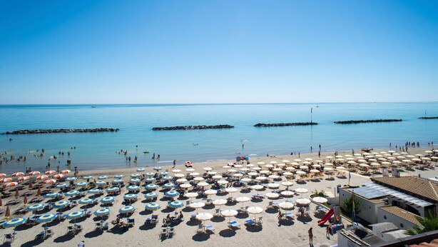 Une plage avec de nombreux parasols et des chaises longues, un ciel bleu dégagé et une mer calme.