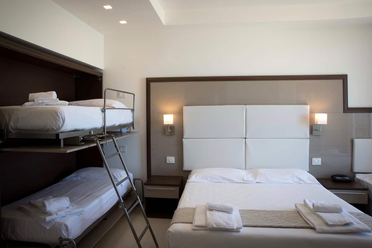 Une chambre d’hôtel avec un lit superposé, un lit simple, une table de chevet avec une lampe et un luminaire fixé au mur.