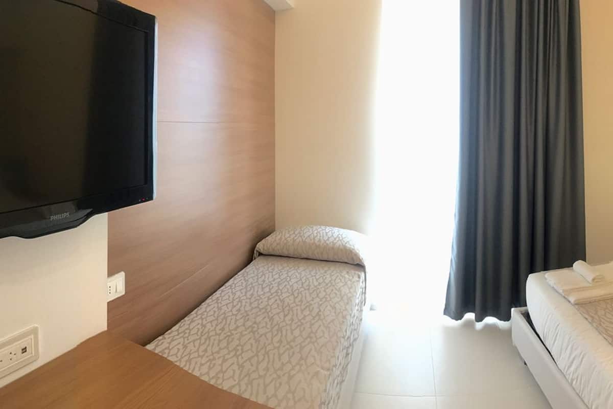 Une chambre d’hôtel avec un lit, un petit lit, une télévision, une table de chevet et une fenêtre avec des rideaux.