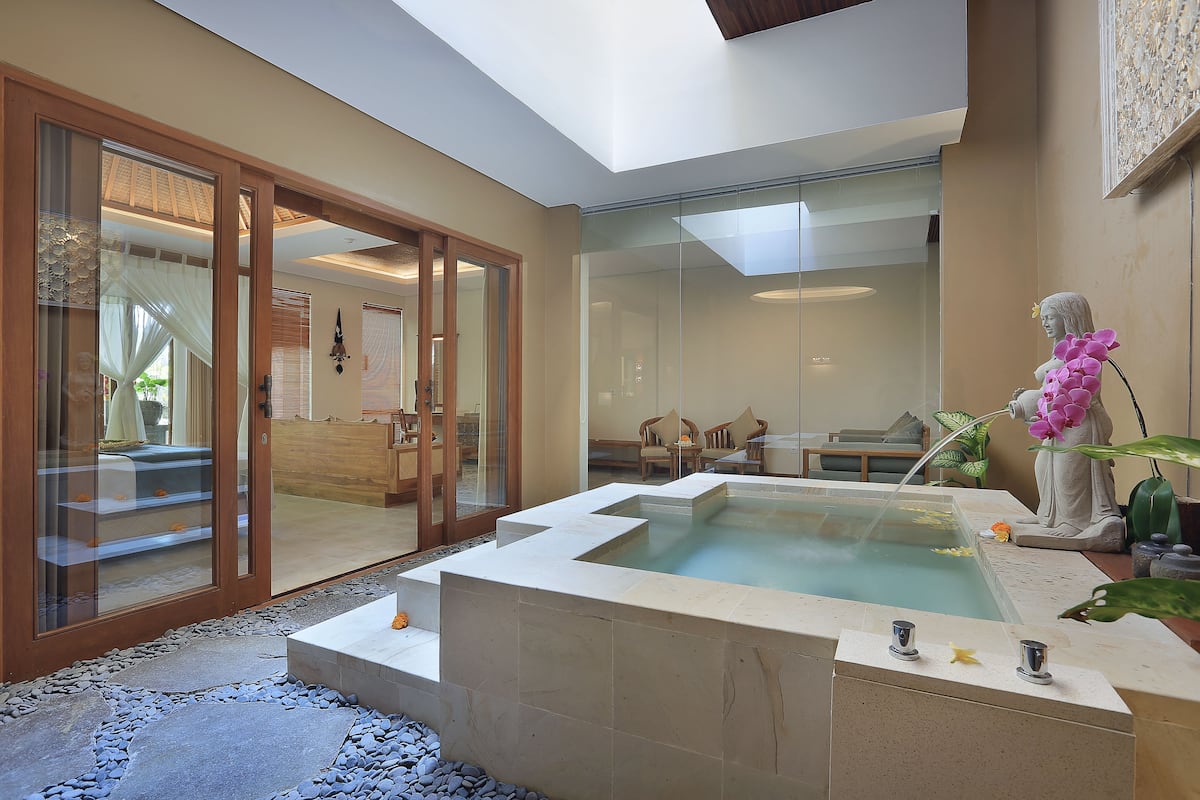 Un espace spa moderne doté d’un jacuzzi, de portes vitrées donnant sur un coin salon et d’une statue représentant une femme tenant des fleurs.