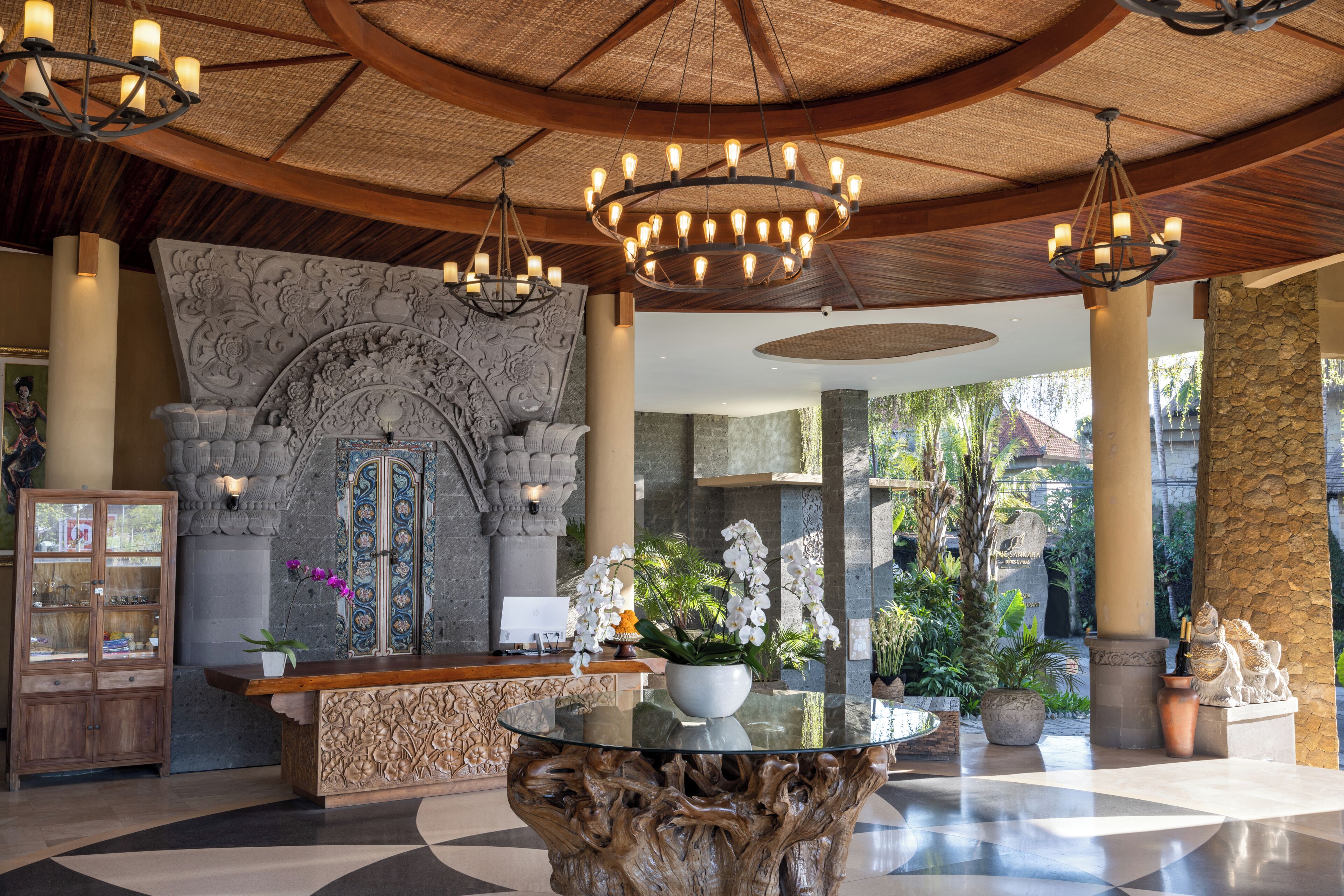 A lobby with a reception desk, a chandelier, a stone wall, and potted plants.