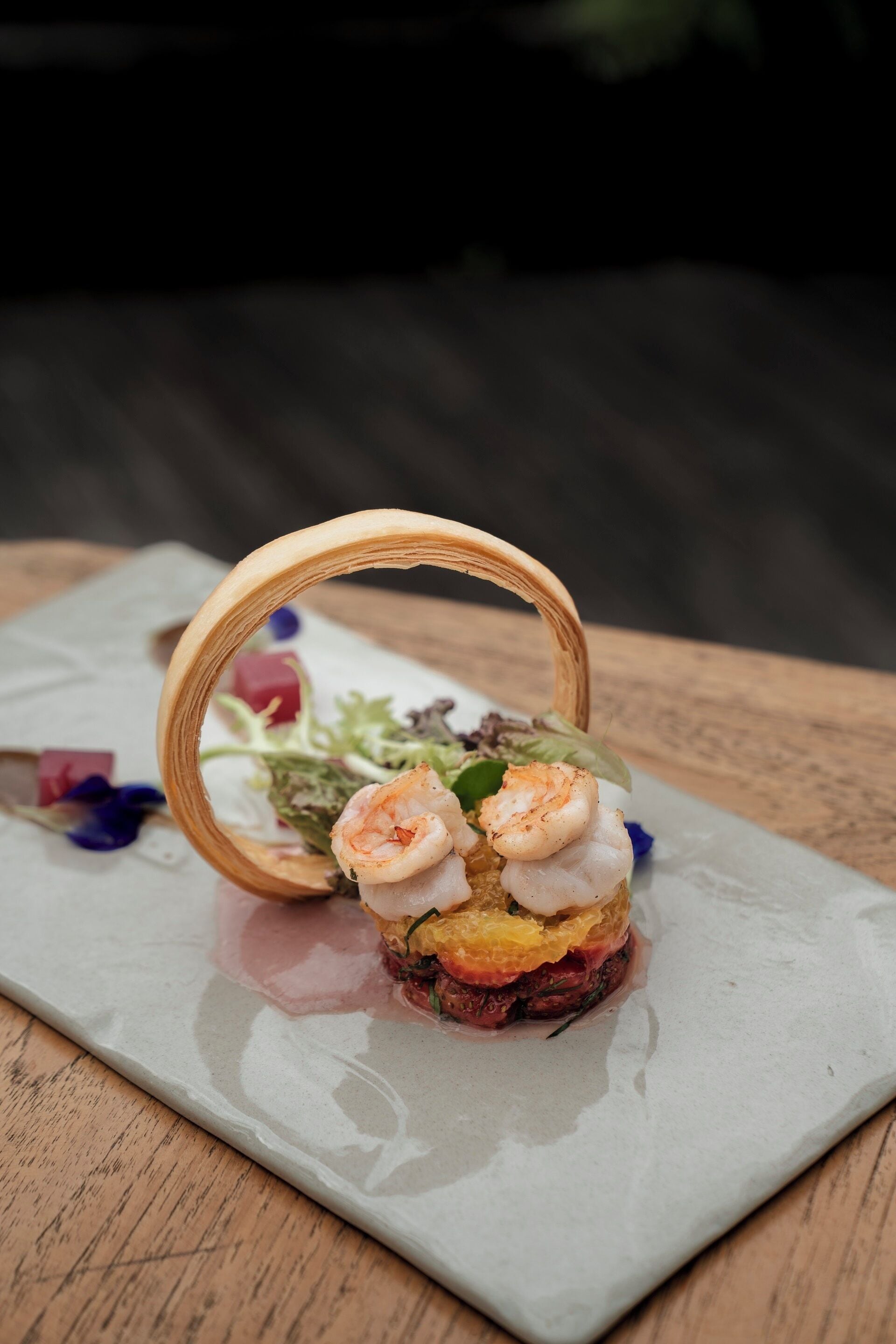 Un plat composé de crevettes servies sur un lit de légumes verts et d’autres ingrédients, présenté dans une assiette rectangulaire.