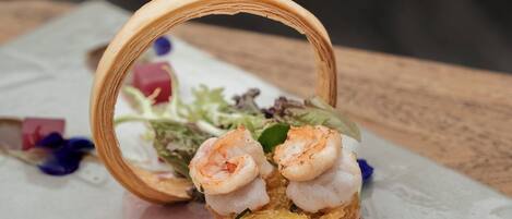 Un plat composé de crevettes servies sur un lit de légumes verts et d’autres ingrédients, présenté dans une assiette rectangulaire.
