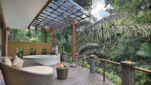 Een houten terras met een rieten bank, een ronde tafel en een whirlpool.
