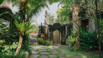 A garden pathway with stone steps leading to a statue, surrounded by lush tropical plants and palm trees.