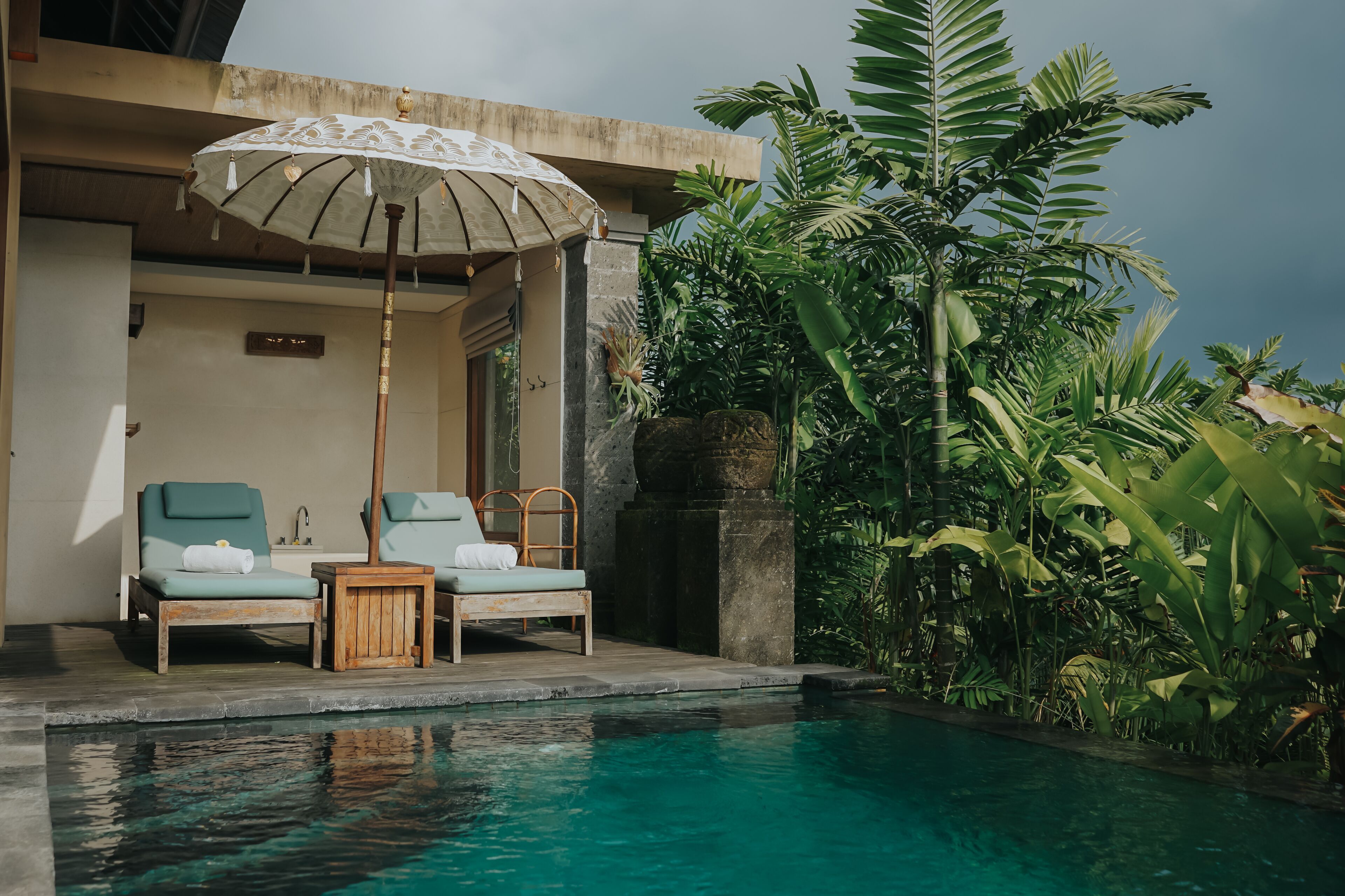 A poolside area with two lounge chairs, a wooden table, and an umbrella.