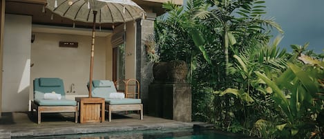 Un espace aménagé au bord de la piscine, comprenant deux chaises longues, une table en bois et un parasol.