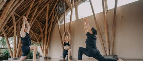A yoga class in a room with a bamboo ceiling and large windows.