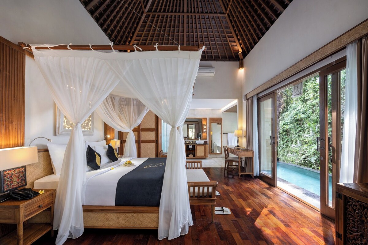 Une chambre spacieuse avec un lit à baldaquin, un bureau en bois et une vue sur l’extérieur.