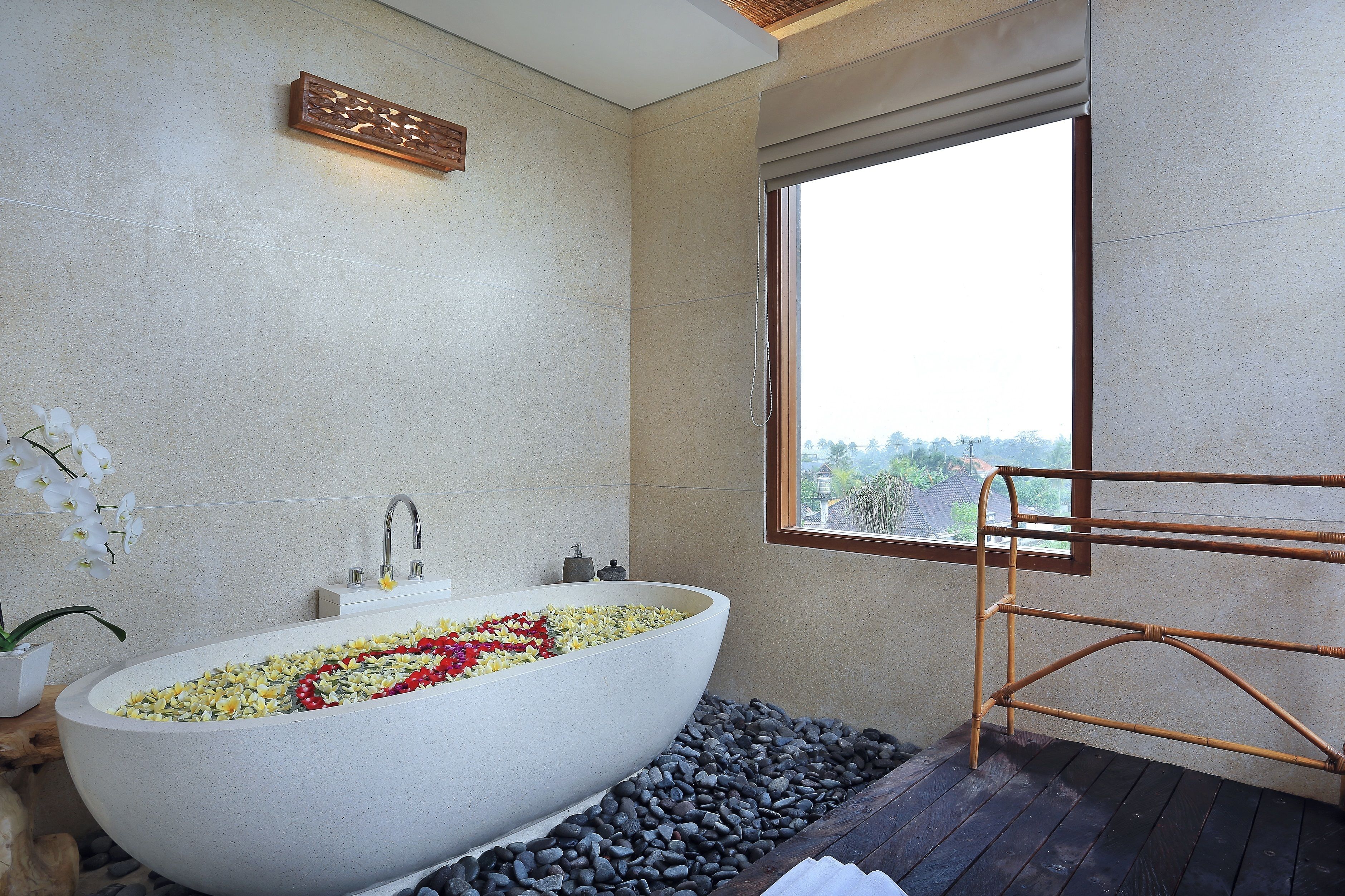 Une salle de bain moderne avec une baignoire îlot remplie de fleurs, une fenêtre offrant une belle vue et un petit escalier en bois pour entrer dans la baignoire.