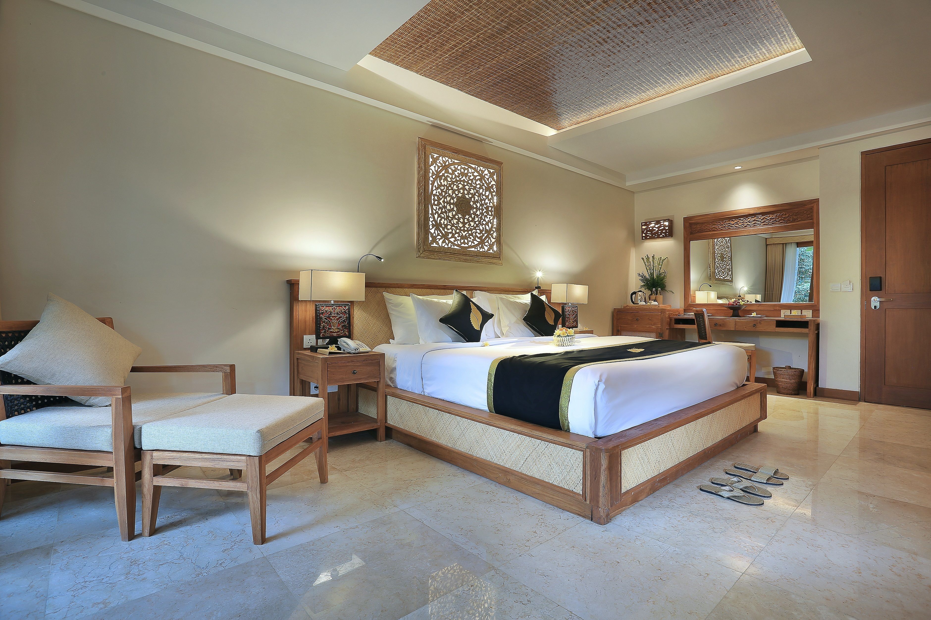 A well-lit bedroom with a large bed, bedside tables, a chair, a desk, and a mirror.
