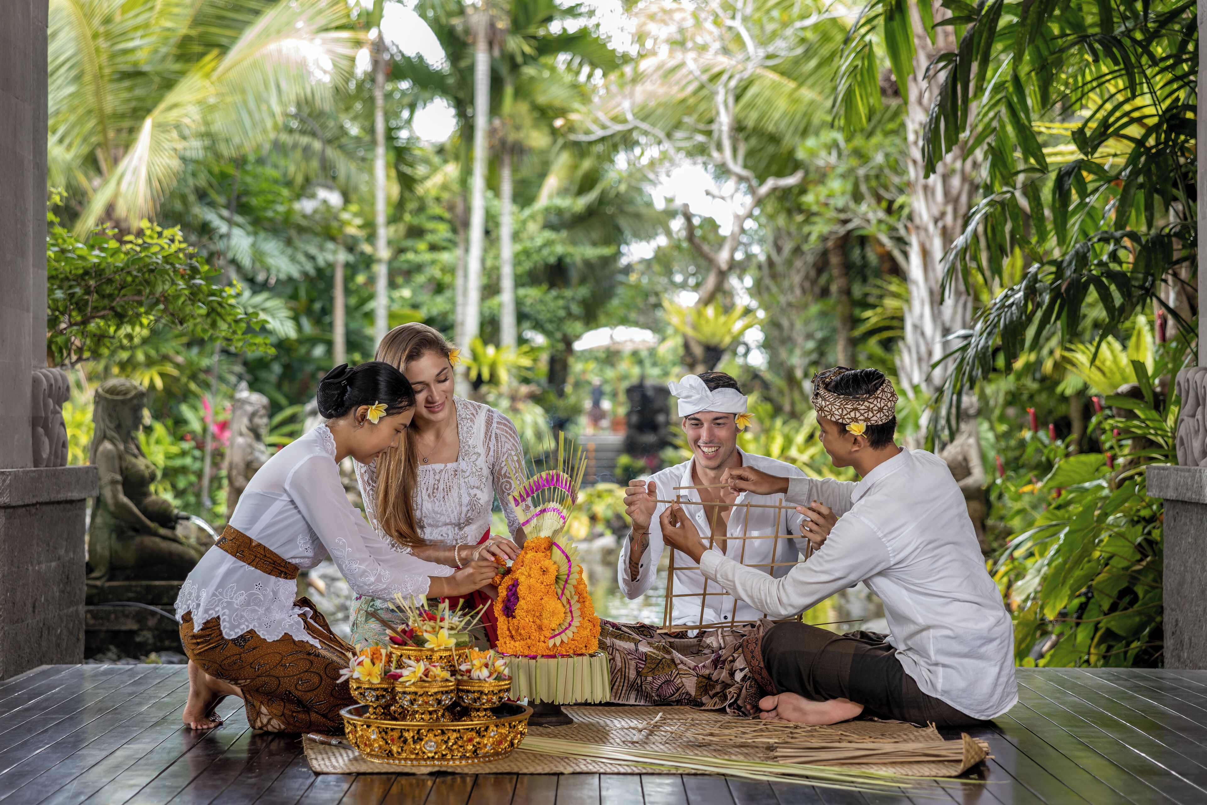 A group of people performing a ritual with offerings on a wooden platform surrounded by lush greenery.