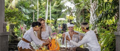 A group of people performing a ritual with offerings on a wooden platform surrounded by lush greenery.
