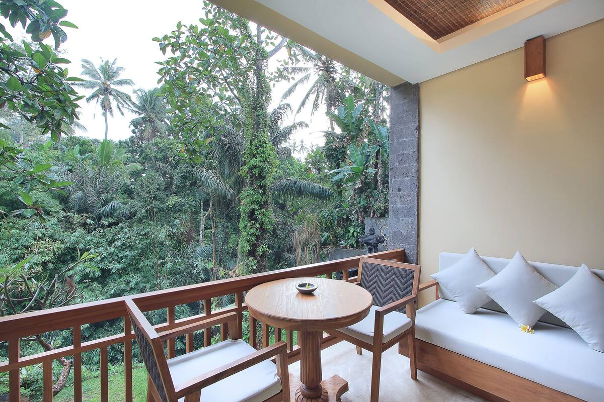 Un balcon avec une table et des chaises en bois, un canapé et une vue sur une végétation luxuriante.