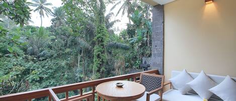 A balcony with a wooden table and chairs, a sofa, and a view of lush greenery.