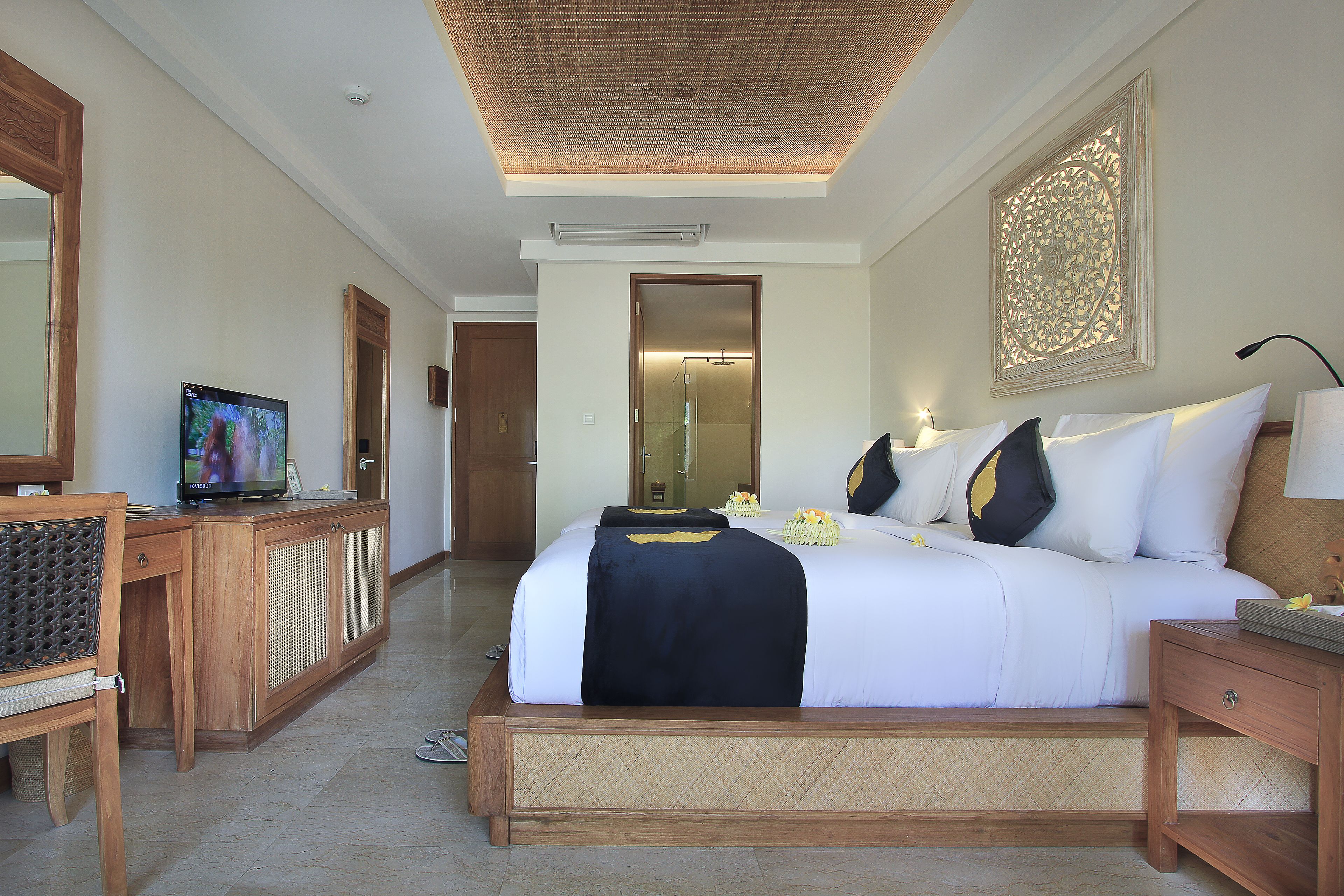 A hotel room with a large bed, a wooden desk, a television, and a decorative wall piece.