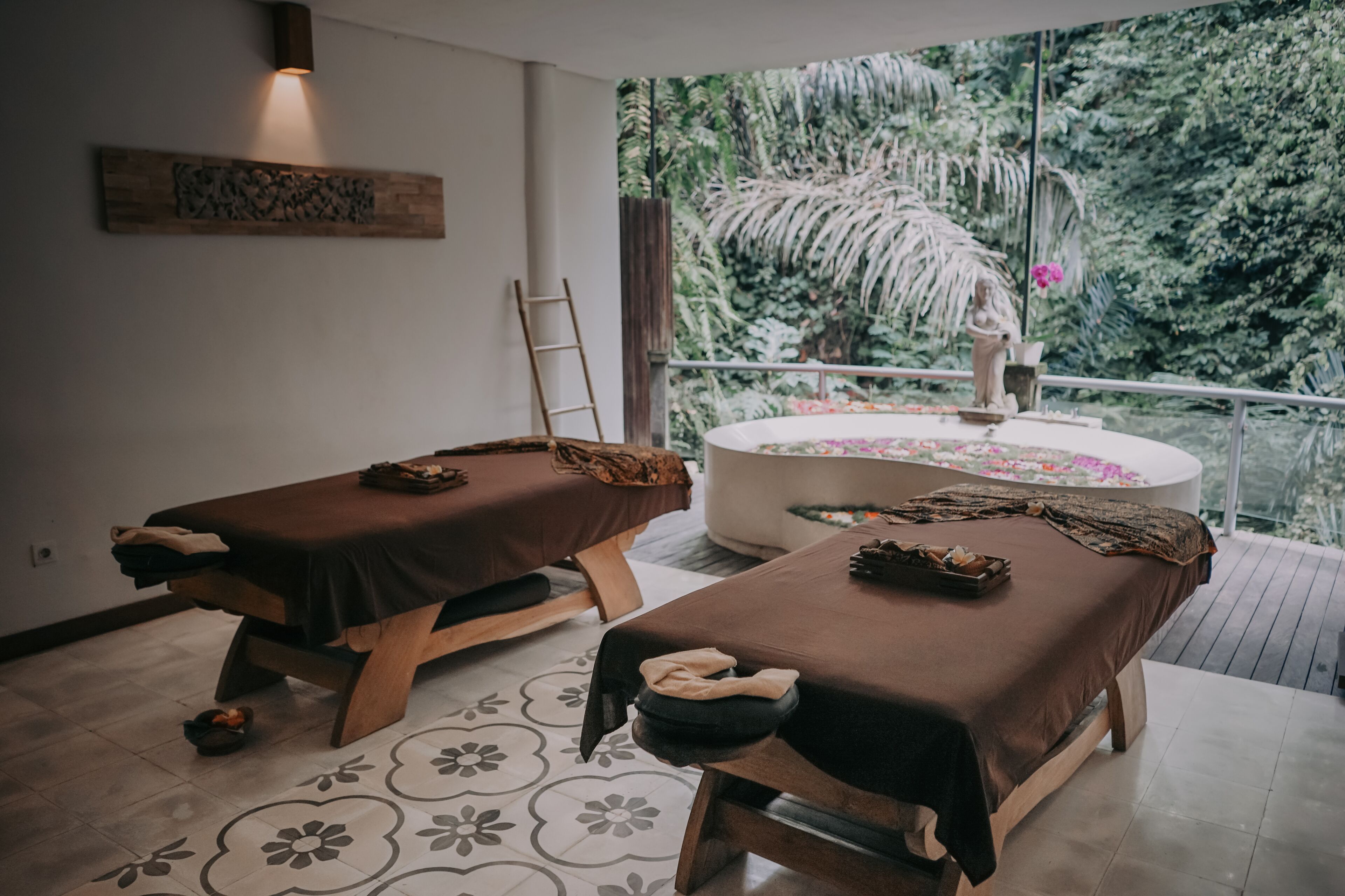 Un cuarto de spa con dos camillas de masaje, una bañera grande y vistas a exuberante follaje.