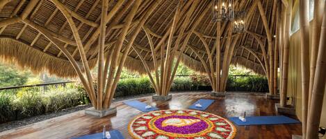 Un espacio interior con techo de bambú, suelo de madera y un arreglo floral circular en el centro.