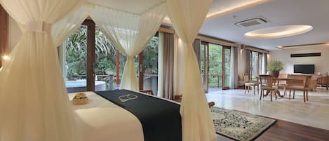 A spacious bedroom with a large bed, a dining area, and a view of greenery.