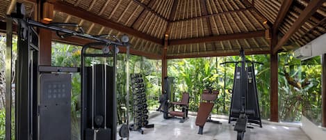 A gym with various exercise equipment, a bench, and a thatched roof structure.