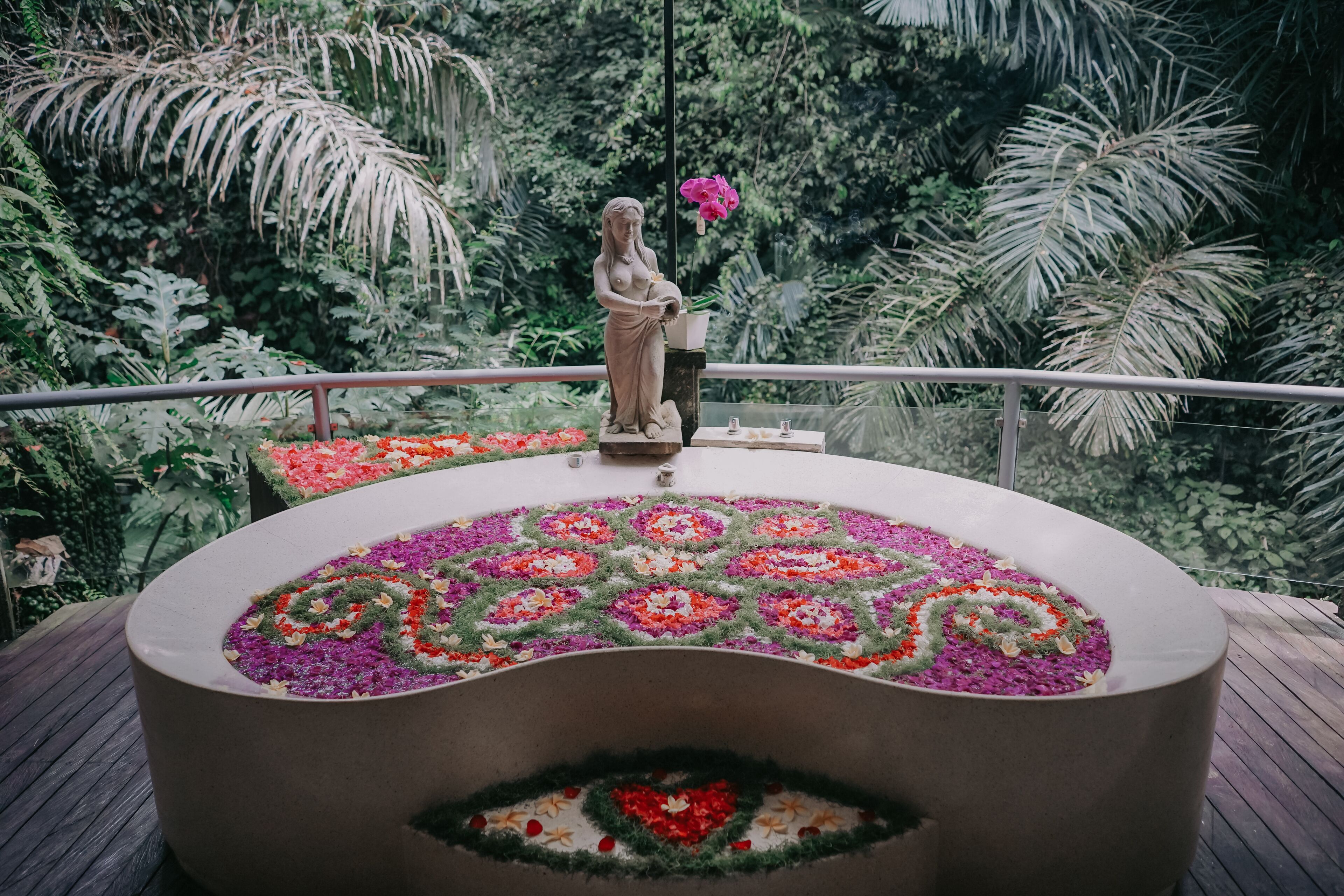 A statue on a circular platform with a floral design in the center, surrounded by lush greenery.
