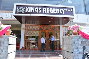 The entrance of Kings Regency hotel with a sign above the door, a security guard, and potted plants.