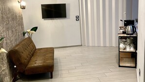A modern living room with a brown sofa, a flat-screen TV, and a small table with kitchenware.