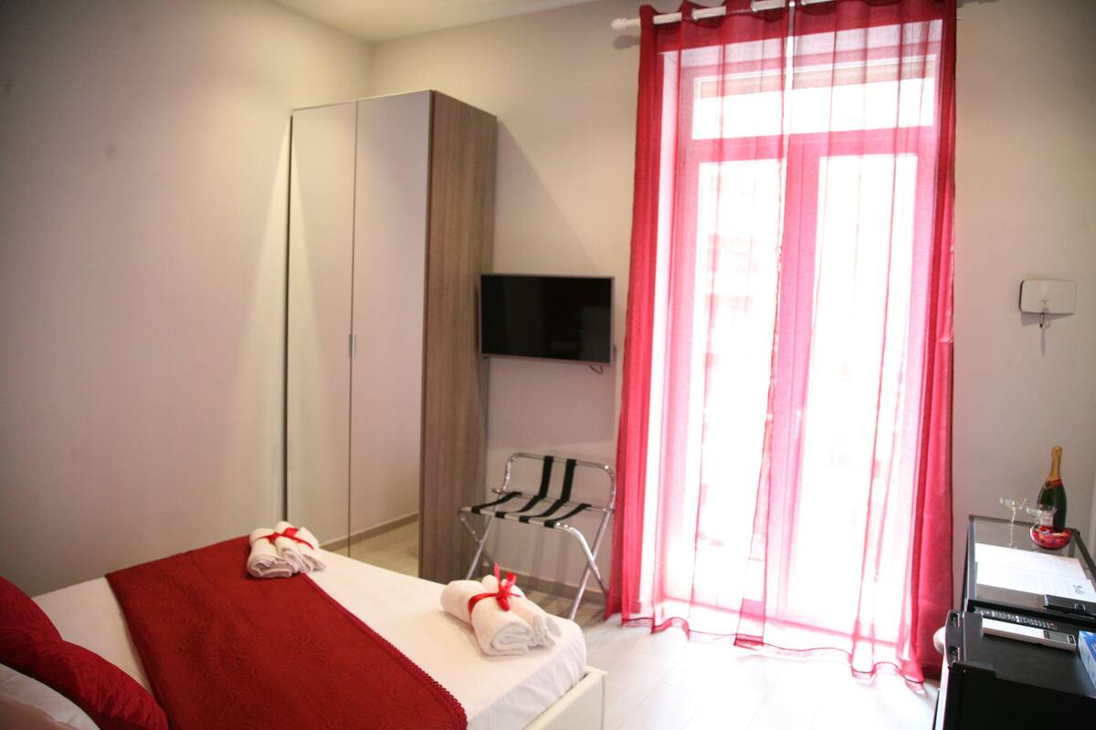 Hotelkamer met een bed, een kledingkast, een televisie, een bureau met een fles en glazen, en een stoel.