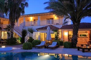 Un hotel de dos pisos con piscina, sillones de descanso y zona de bar.