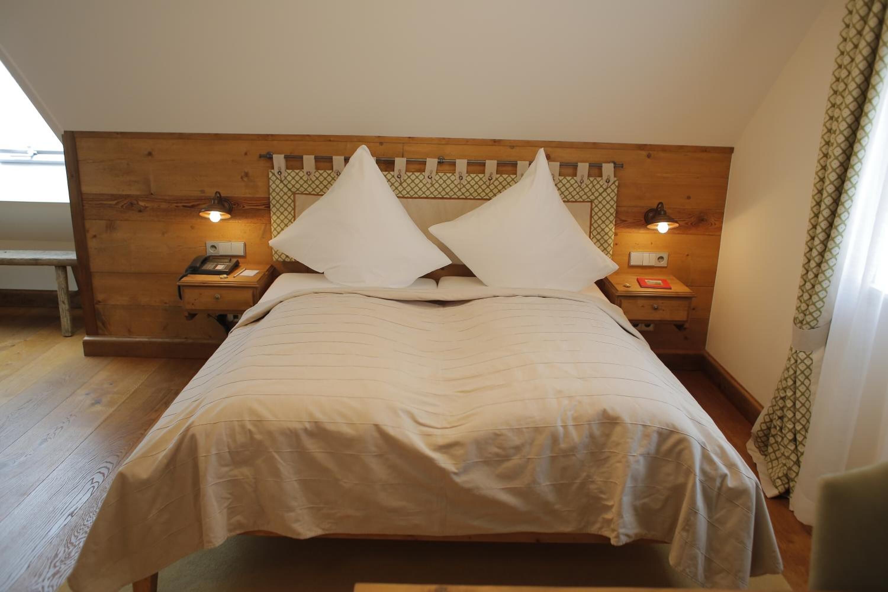Uma cama bem arrumada com cabeceira de madeira, duas mesas de cabeceira com luminárias e um banco no canto.