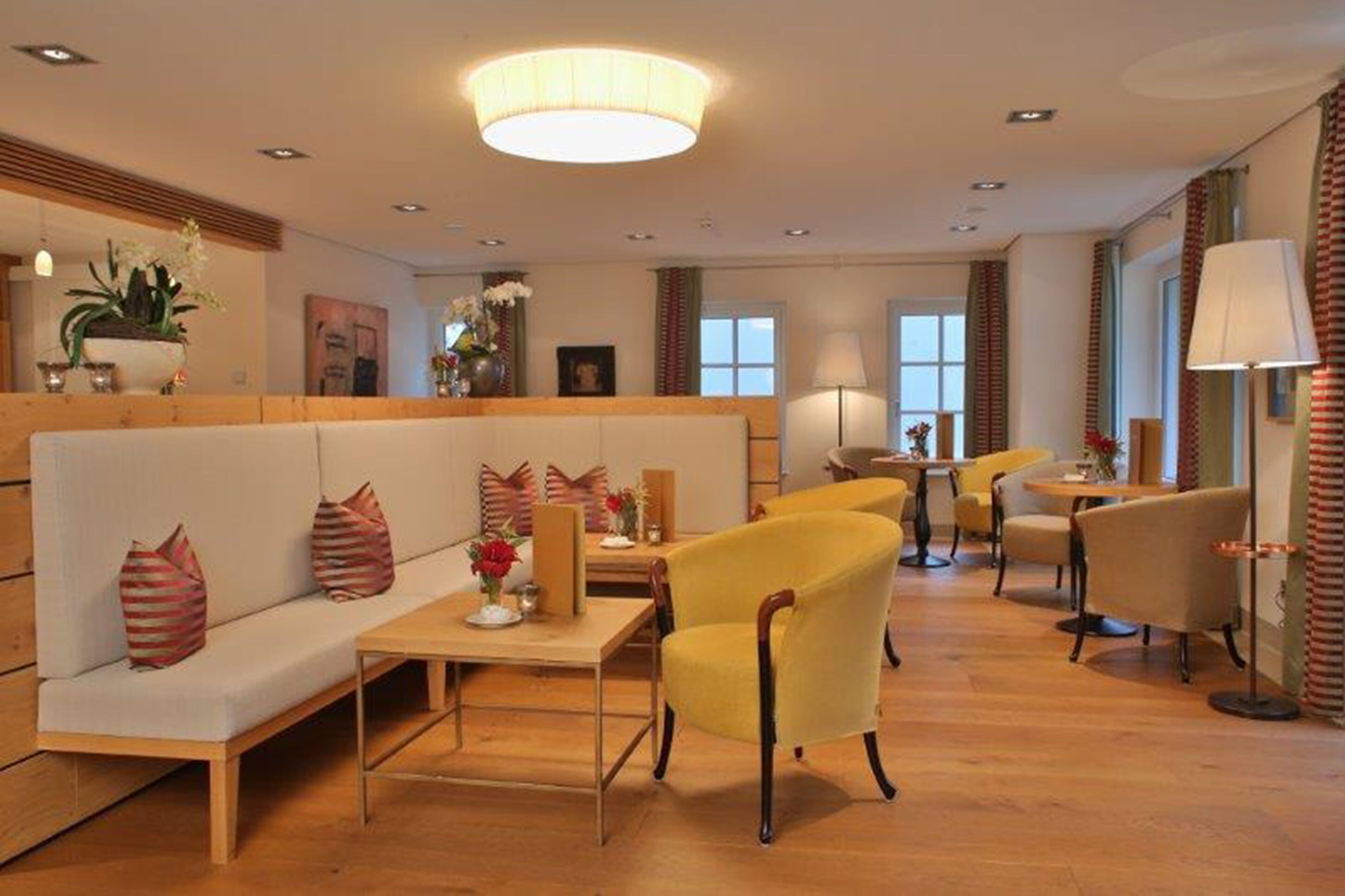 A modern hotel lobby with a sofa, yellow chairs, a round table, and a chandelier.