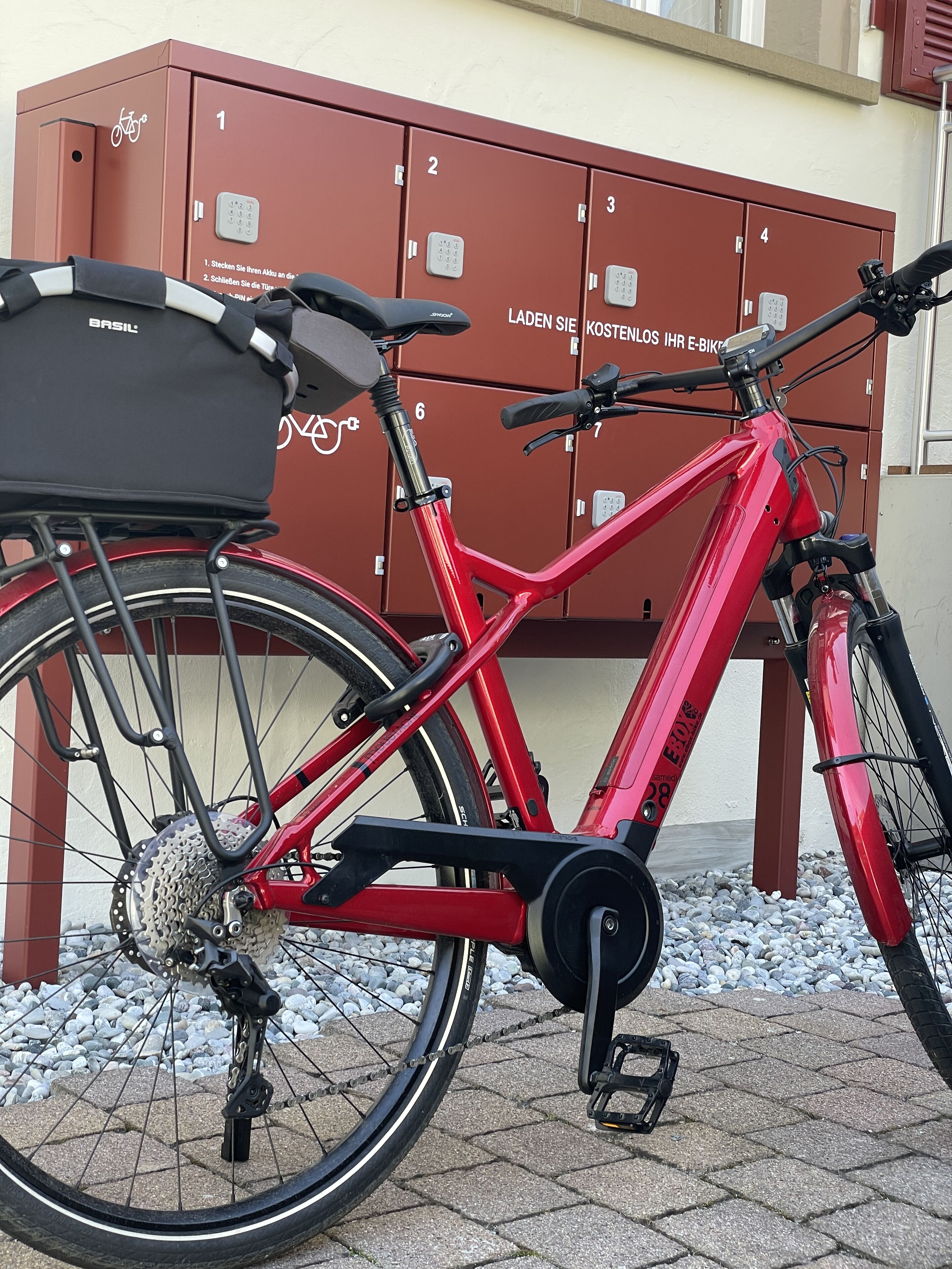Una bicicleta roja estacionada junto a una hilera de taquillas numeradas.