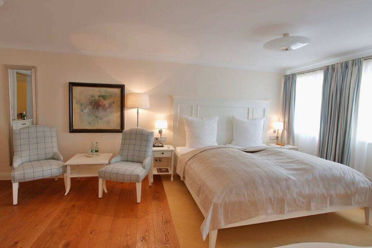 Une chambre d’hôtel avec un lit, deux chaises, une petite table, une lampe et un tableau au mur.