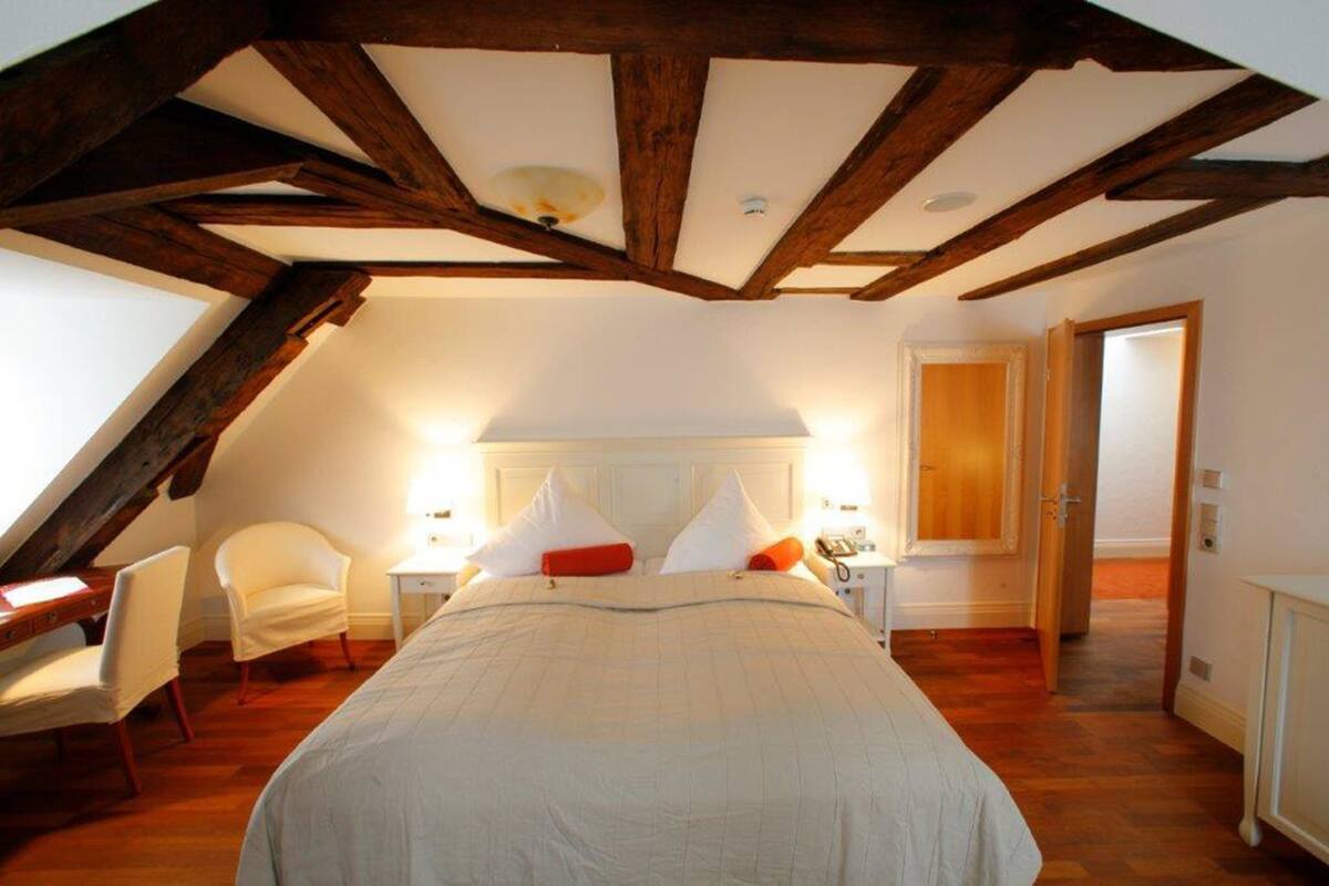 Une chambre avec un plafond en pente, un lit avec une literie blanche, une table de chevet avec une lampe et une chaise.