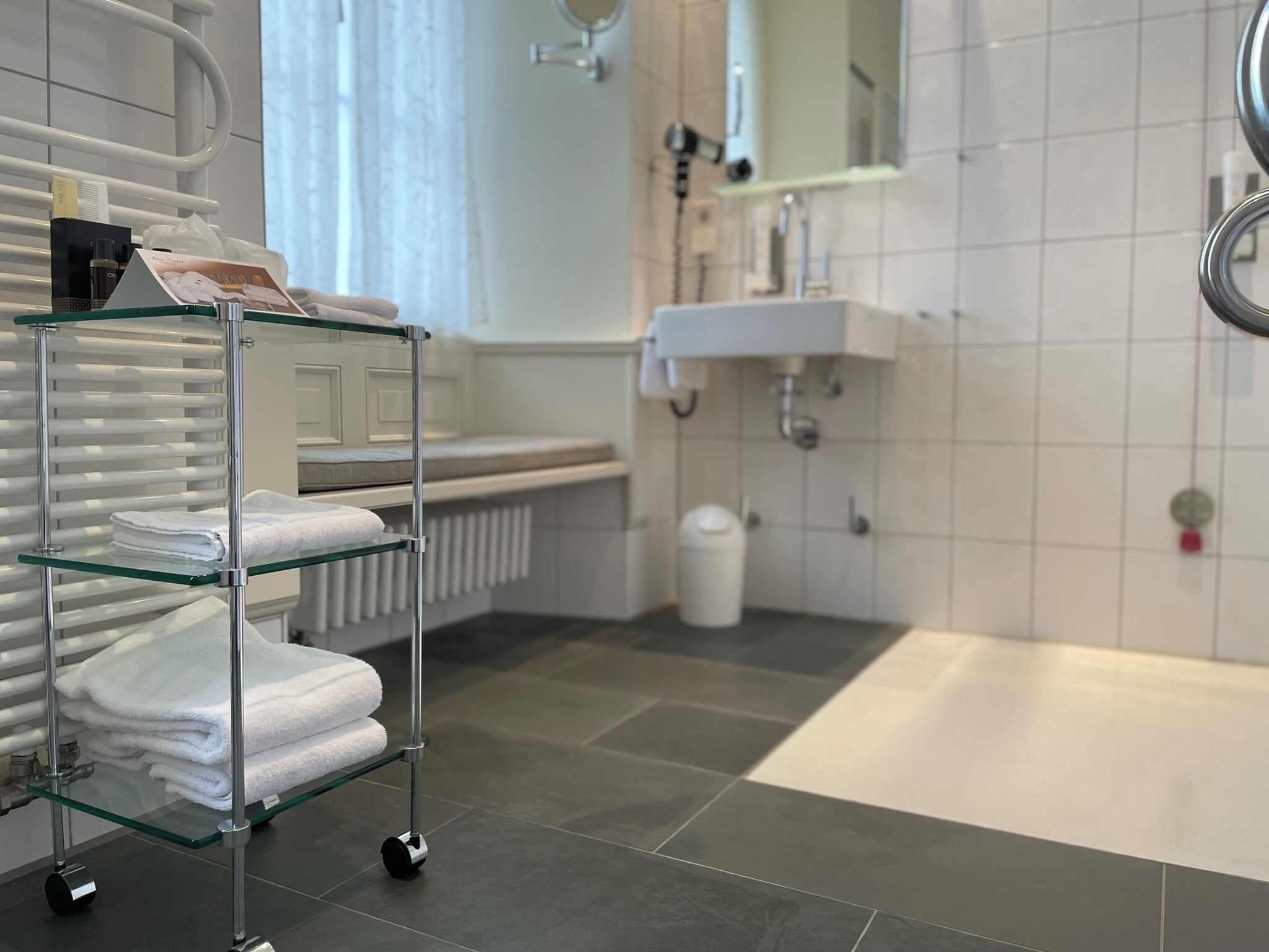 Un baño moderno con repisas de vidrio que sostienen toallas, un lavamanos blanco y una bañera.