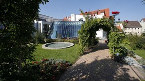 Een tuin met een geplaveid pad, een fontein en een modern gebouw met een glazen gevel.
