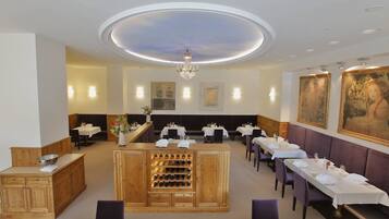 A restaurant with a central bar area, multiple dining tables, and a ceiling with a circular light fixture.