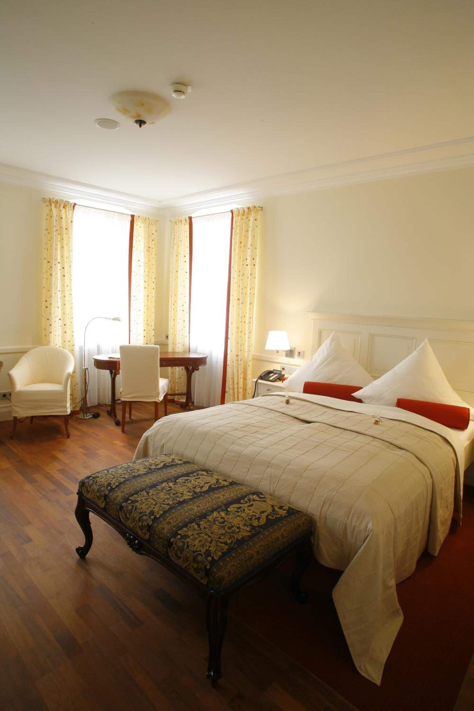 A hotel room with a large bed, a desk, a chair, and a small table.