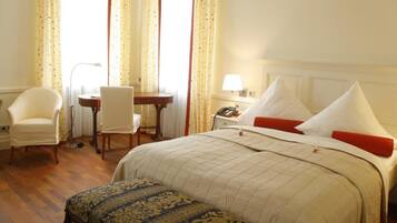 A hotel room with a large bed, a desk, a chair, and a small table.
