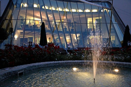 A modern building with a glass facade, a fountain, and red flowers in the foreground.