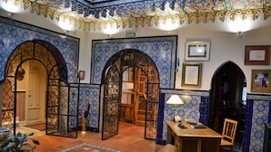 Une pièce décorée de motifs complexes en carreaux bleus et blancs, une porte en bois, une table avec une lampe et un banc.