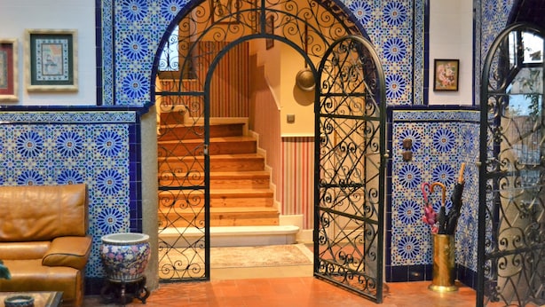Une pièce avec un mur aux motifs bleus et blancs, un escalier en bois, un canapé en cuir marron et un vase décoratif.