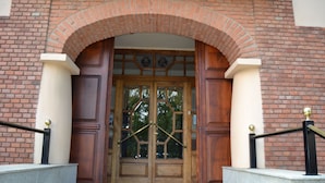 Une entrée d’immeuble en briques, avec une porte en bois, une rambarde en métal et un rebord en pierre.