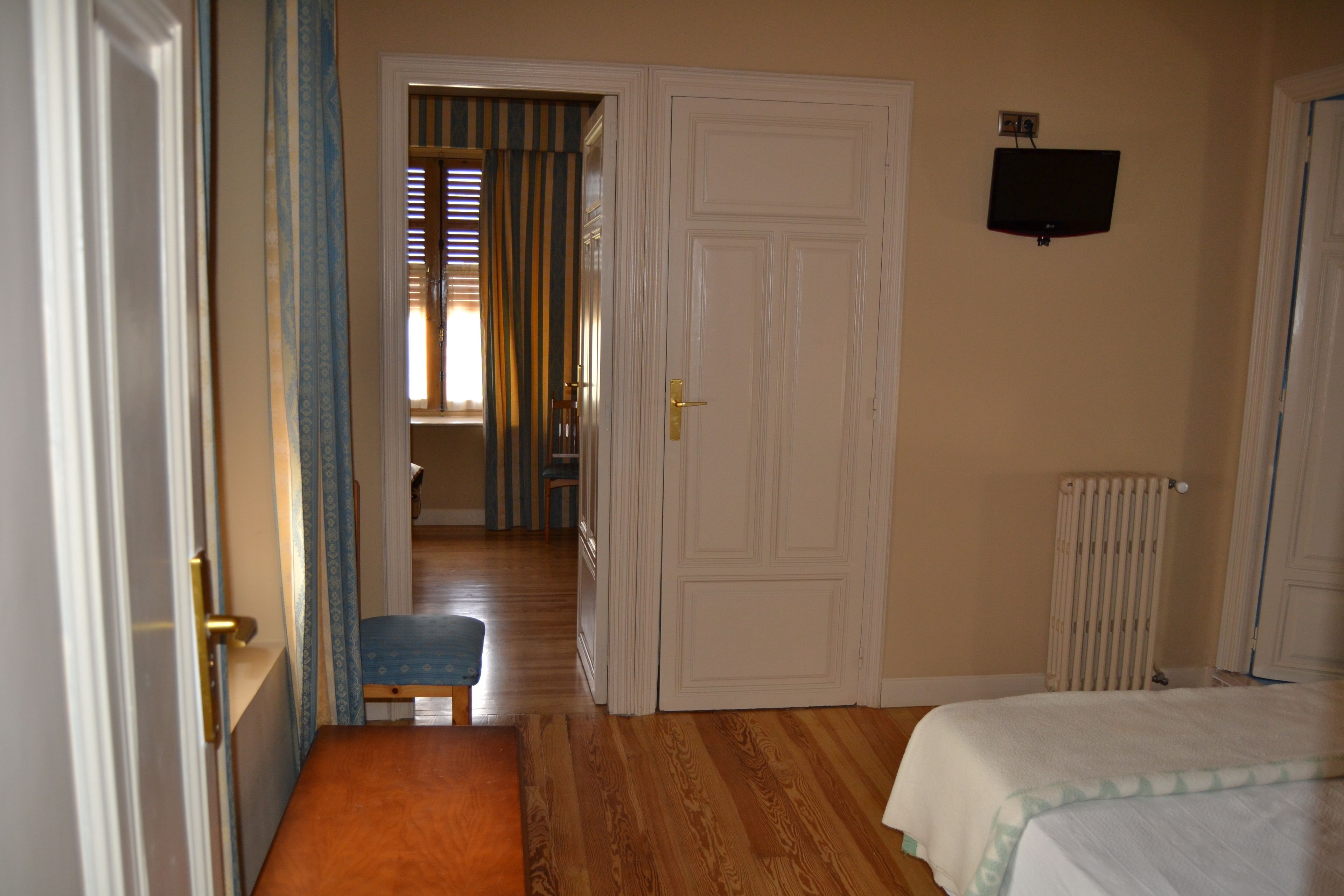 Un dormitorio con piso de madera, una cama, un radiador y un televisor en la pared.