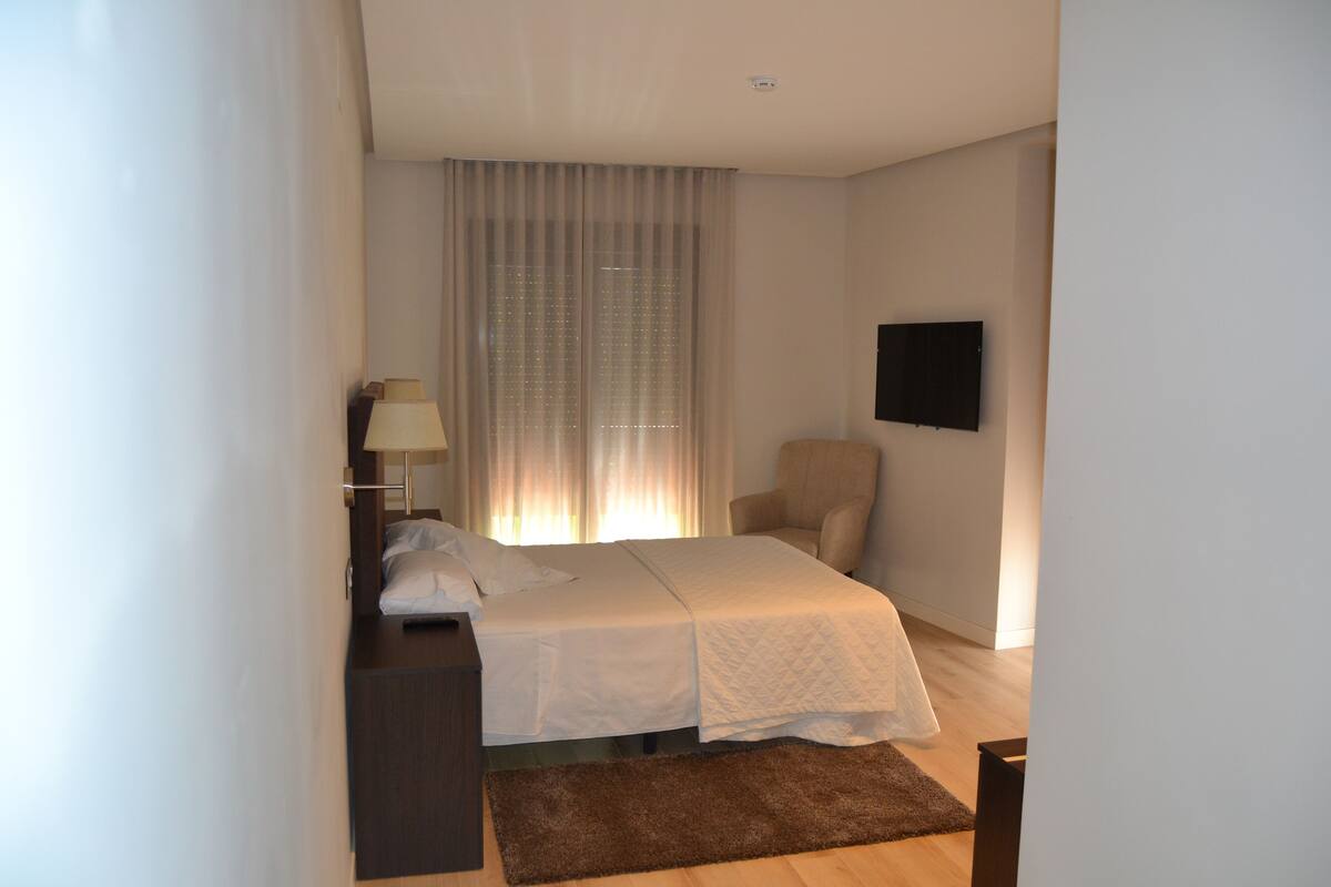 Un dormitorio con cama, una silla, un escritorio, una lámpara y un televisor.